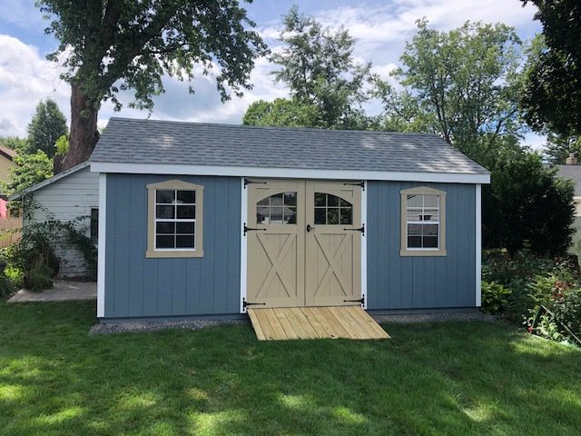A blue Smartside shed in a yard surrounded by trees.